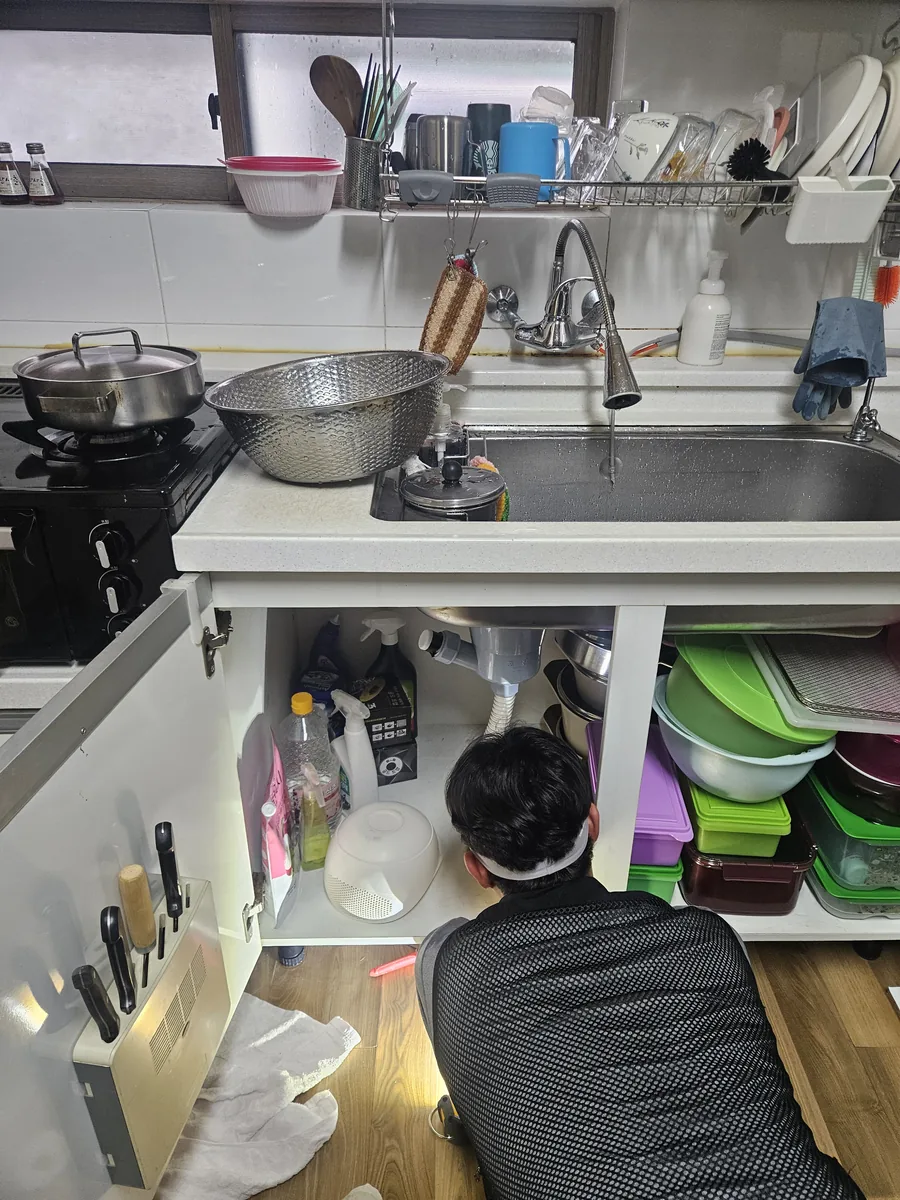 싱크대 아래로 들어가 배관을 확인하고 있습니다.